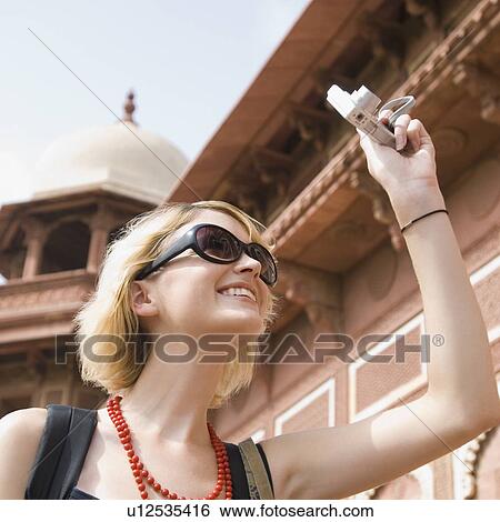 Stock Photograph - Close-up of a young woman taking a picture with a digital camera, Taj Mahal, Agra, Uttar Pradesh, India. Fotosearch