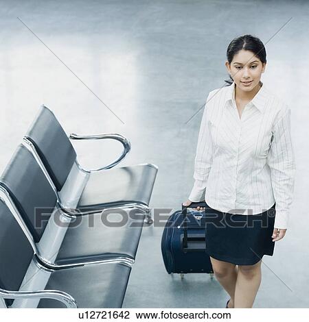 Stock Image - High angle view of a businesswoman pulling her luggage at an airport. Fotosearch