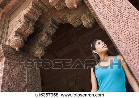 Stock Photo - Low angle view of a young woman standing under an arch, Taj Mahal, Agra, Uttar Pradesh, India. Fotosearch