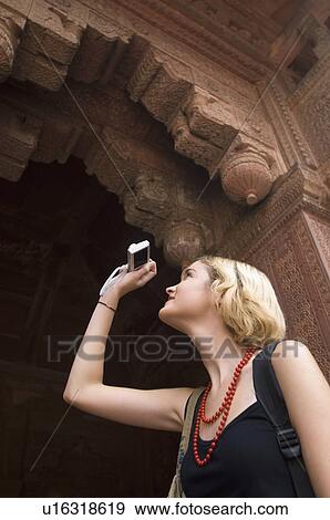 Stock Photo - Low angle view of a young woman taking a picture with a digital camera, Taj Mahal, Agra, Uttar Pradesh, India. Fotosearch