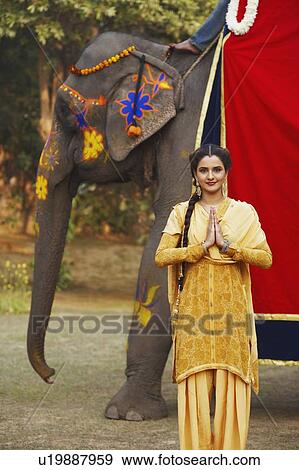 Stock Photo - Portrait of a young woman greeting in front of an elephant. Fotosearch