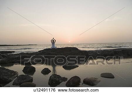 Rear view of a woman practicing yoga on the coast View Large Photo Image Stock Photograph - Rear view of a woman practicing yoga on the coast. Fotosearch