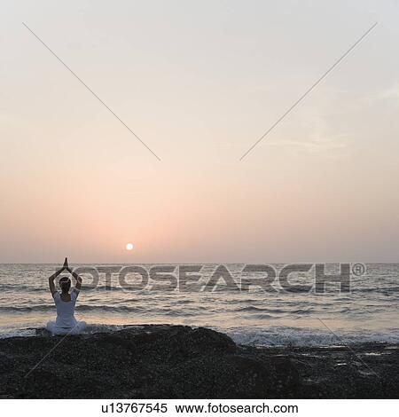 Rear view of a woman practicing yoga on the coast View Large Photo Image Stock Photography - Rear view of a woman practicing yoga on the coast. Fotosearch
