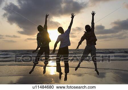 Rear view of three young men jumping with their hands raised on the beach View Large Photo Image Stock Image - Rear view of three young men jumping with their hands raised on the beach. Fotosearch