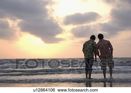 Stock Photograph - Rear view of two young men walking on the beach. Fotosearch