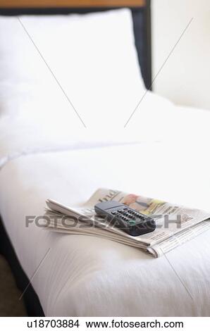 Remote control and a newspaper on the bed in a hotel room View Large Photo Image Picture - Remote control and a newspaper on the bed in a hotel room. Fotosearch