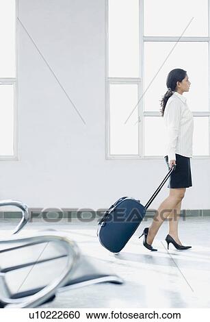 Side profile of a businesswoman pulling her luggage at an airport View Large Photo Image Stock Image - Side profile of a businesswoman pulling her luggage at an airport. Fotosearch
