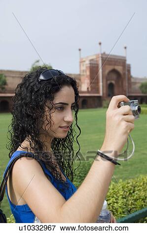 Stock Photo - Side profile of a young woman taking a picture with a digital camera, Taj Mahal, Agra, Uttar Pradesh, India. Fotosearch