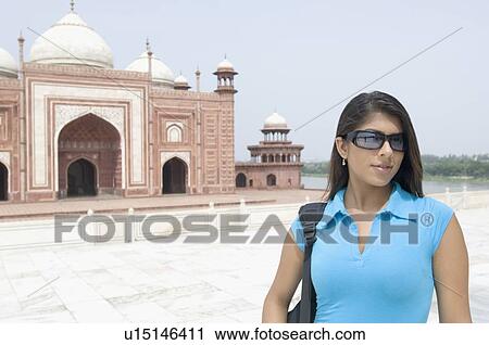 Stock Image - Young woman standing in front of a mausoleum, Taj Mahal, Agra, Uttar Pradesh, India. Fotosearch