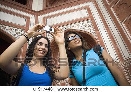 Low angle view of a young woman taking a picture with her friend standing beside her, Taj Mahal, Agra, Uttar Pradesh, India View Large Photo Image Stock Image - Low angle view of a young woman taking a picture with her friend standing beside her, Taj Mahal, Agra, Uttar Pradesh, India. Fotosearch