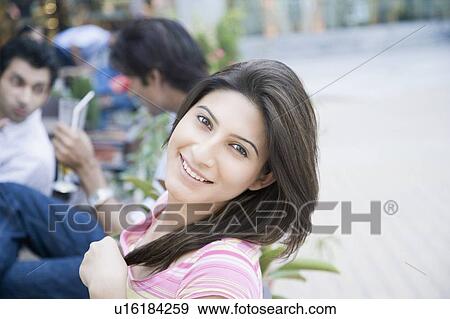 Stock Photo - Portrait of a young woman smiling with two young men in the background. Fotosearch