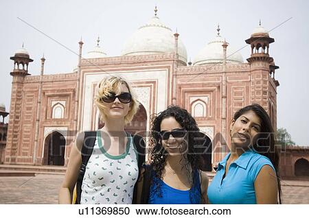 Stock Image - Portrait of three young women smiling in front of a mausoleum, Taj Mahal, Agra, Uttar Pradesh, India. Fotosearch