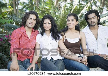 Portrait of two young couples sitting on a ledge and smiling View Large Photo Image Picture - Portrait of two young couples sitting on a ledge and smiling. Fotosearch