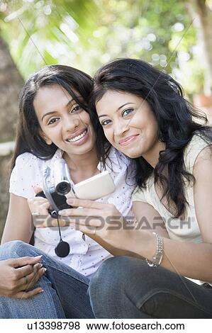 Stock Photo - Portrait of two young women holding a digital video camera and smiling. Fotosearch