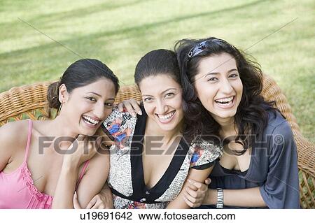 Stock Image - Three young women sitting on a couch in a park and laughing. Fotosearch