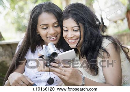 Stock Image - Two young women looking at a digital video camera and smiling. Fotosearch