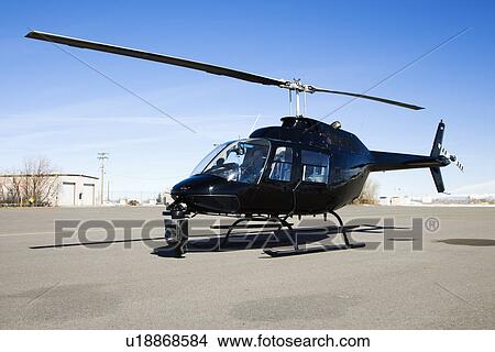 Picture - Black helicopter with camera mounted on front parked at airport tarmac.. Fotosearch