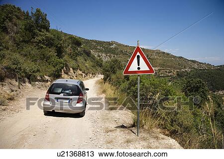 Stock Image - Car heading down dirt road with caution sign.. Fotosearch