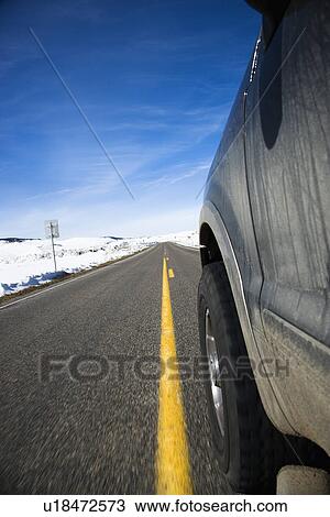 Stock Image - Perspective shot of SUV driving down road in snowy Colorado during winter.. Fotosearch