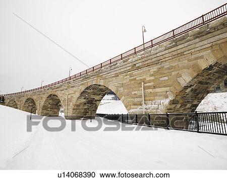 Stock Image - Scene of stone bridge over over snow covered road.. Fotosearch