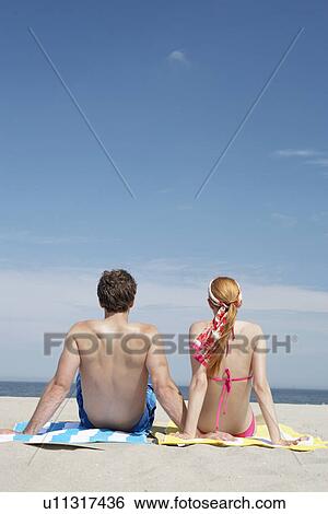 Young couple sitting at beach and looking at view (rear view) View Large Photo Image Stock Photograph - Young couple sitting at beach and looking at view (rear view). Fotosearch
