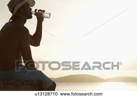 Young man drinking water on beach View Large Photo Image Stock Image - Young man drinking water on beach. Fotosearch