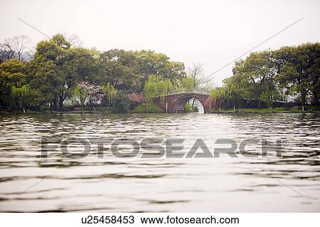 Stock Image - China, Zhejiang Province, Hangzhou, West Lake, stone bridge in the distance. Fotosearch
