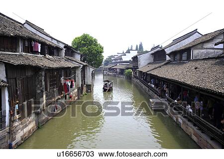 Stock Image - Asia, China, Zhejiang Province, Wuzhen, row boat in canal. Fotosearch