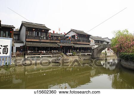 Stock Image - China, Zhejiang Province, Xitang Town, traditional architecture and bridge reflected in water. Fotosearch