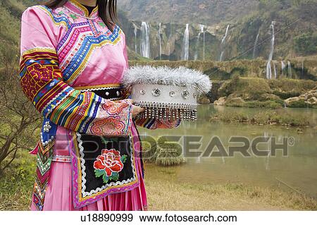 Stock Photo - China, Yunnan Province, Luoping County, Buyi National Minority, Young woman in traditional clothing holding hat. Fotosearch
