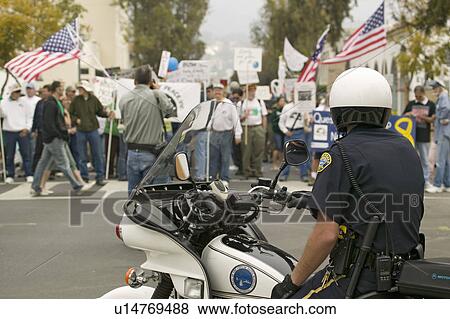 Stock Photo - A motorcycle policeman looks at protesters against George W. Bush and the Iraq War at an anti-Iraq War protest march in Santa Barbara, California on March 17, 2007. Fotosearch