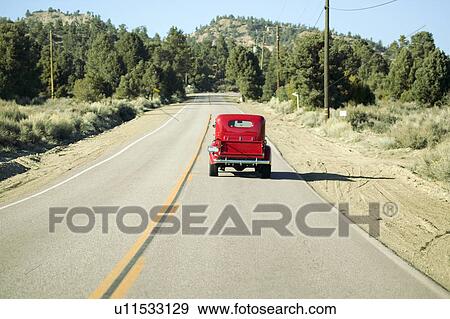 Stock Photo - A restored bright Red Roadster hotrod pickup truck, mid-30's, drives rural highway in Kern County near Lockwood Valley, CA. Fotosearch