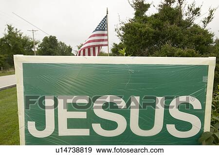 Stock Photo - A sign reads "Jesus" promoting the Christian point of view alongside an American Flag, representing the separation of Church and State in St. Louis County, Missouri. Fotosearch