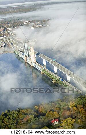 Picture - Aerial view of fog over Bath Iron Works and Kennebec River in Maine. Bath Iron Works is a leader in surface combatant design and construction with a $27 million dollar contract from the Navy for maintenance, repair and upgrades to Aegis destroyers.. Fotosearch