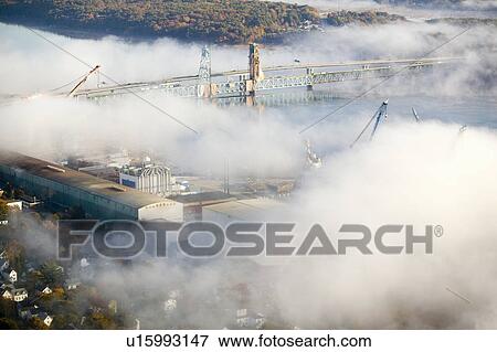 Stock Photo - Aerial view of fog over Bath Iron Works and Kennebec River in Maine. Bath Iron Works is a leader in surface combatant design and construction with a $27 million dollar contract from the Navy for maintenance, repair and upgrades to Aegis destroyers.. Fotosearch