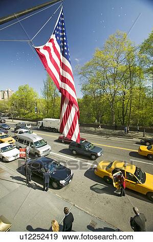 Stock Photo - American Flag flies over Central Park in spring with yellow taxies in front of Helmsely Park Lane, Manhattan, New York City, NY. Fotosearch