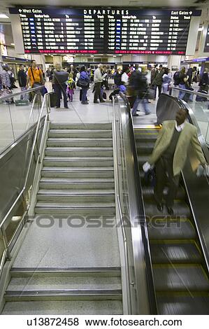 Amtrak train travelers stand in line under Departures sign, while a man goes down escalator at Penn Station, New York City, Manhattan, New York View Large Photo Image Stock Photo - Amtrak train travelers stand in line under Departures sign, while a man goes down escalator at Penn Station, New York City, Manhattan, New York. Fotosearch