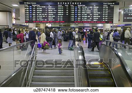 Stock Photo - Amtrak train travelers stand in line under Departures sign, while a man goes down escalator at Penn Station, New York City, Manhattan, New York. Fotosearch