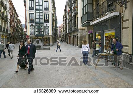 Stock Photo - Business people take lunchtime walk as painter paints in Bilbao (Bilbo), the North Coast of Spain. Fotosearch