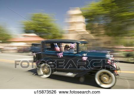 Stock Photograph - Festive decorated antique automobile makes its way down main street during a Fourth of July parade in Ojai, CA. Fotosearch