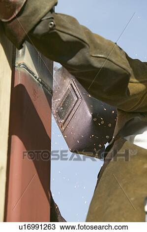 Stock Image - Glowing light of welder welding steel beam on California home. Fotosearch