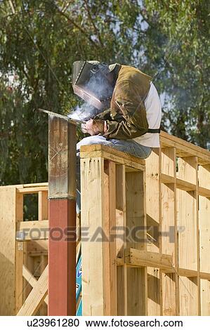 Stock Image - Glowing light of welder welding steel beam on California home. Fotosearch