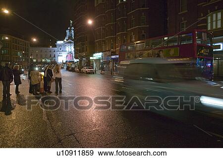 Stock Photo - Hailing a cab on wet night streets of West End of London's theater district with double decker bus driving by, England. Fotosearch