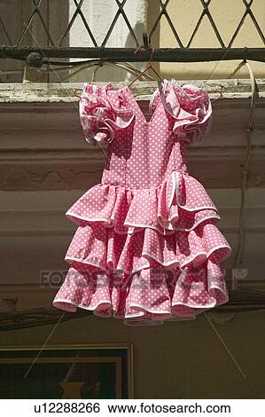 Stock Photograph - Pink flamenco dress for little girl hangs in Centro old district of Sevilla Spain. Fotosearch