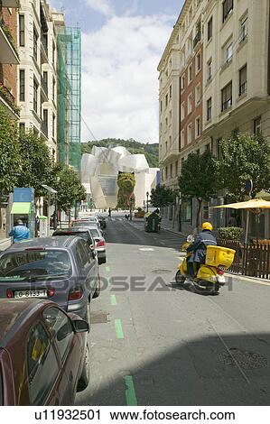 Stock Image - Yellow motorcycle drives toward The Guggenheim Museum of Contemporary Art of Bilbao (Bilbo), located on the North Coast of Spain in the Basque region. Nicknamed "The Hole", this is a contemporary museum built of titanium, limestone and glass and was desig. Fotosearch