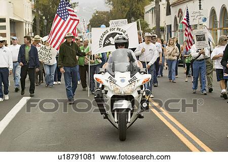 Stock Image - A motorcycle policeman leads parade of protesters against George W. Bush and the Iraq War at an anti-Iraq War protest march in Santa Barbara, California on March 17, 2007. Fotosearch