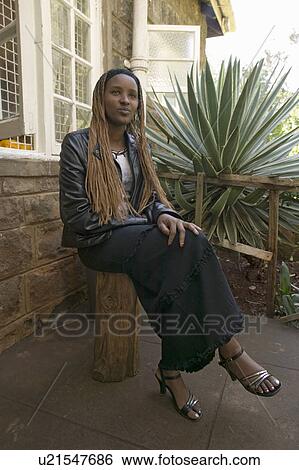 Stock Photograph - African woman with braded hair sits in front of Karen Blixen Museum and Blixen home in Nairobi, Kenya, Africa. Fotosearch