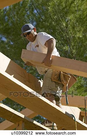 Stock Image - Carpenter lifts central beam of framing process in Southern California. Fotosearch
