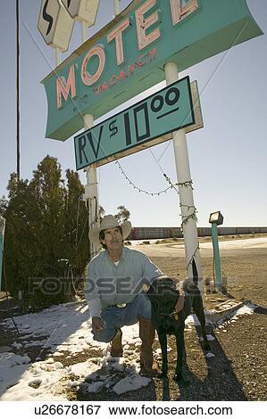 Stock Photo - Cowboy and his dog kneel down in front of the Sands Motel Sign with RV Parking for $10, located at the intersection of Route 54 & 380 in Carrizozo, New Mexico. Fotosearch