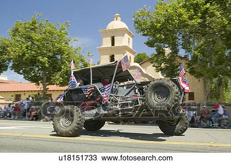 Stock Image - Flag adorned jeep demonstrates 4 wheel maneuvers as it makes its way down main street during a Fourth of July parade in Ojai, CA. Fotosearch